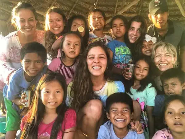 niños y niñas de un país tercermundista sonriendo a cámara junto a una voluntaria extranjera